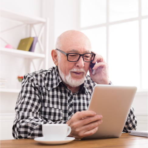an elderly man talks on phone while holding tablet