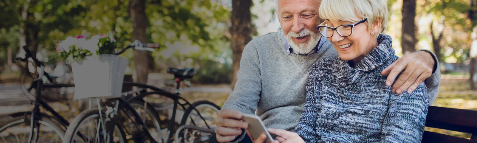 elderly couple sitting on park bench and looking at mobile phone