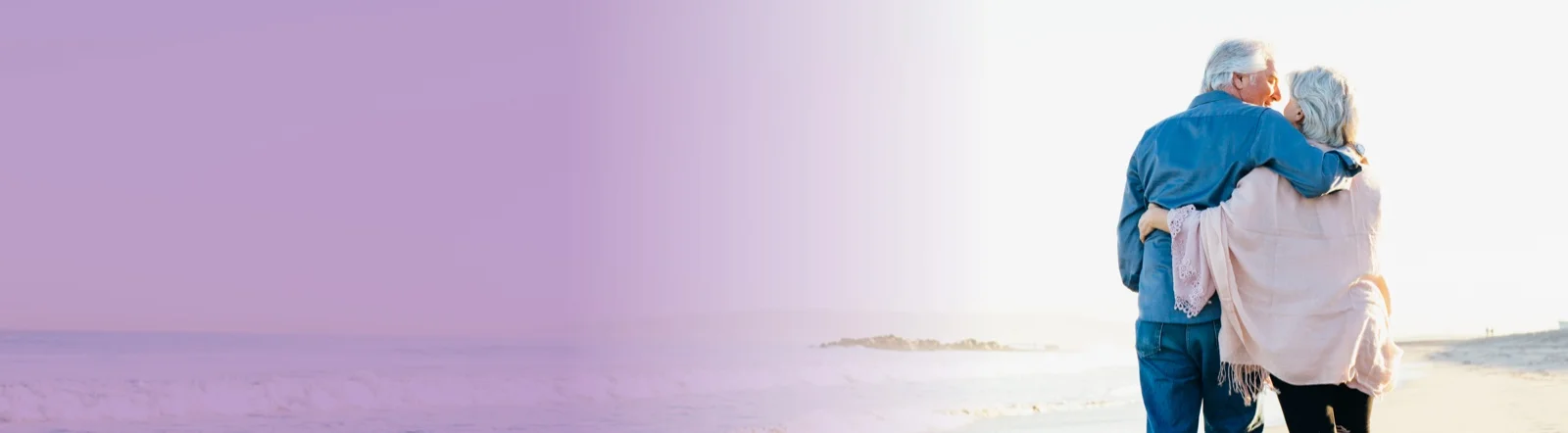 elderly couple looks lovingly at one another while walking on beach